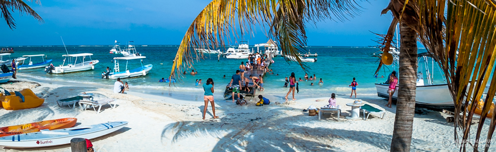 Tourists enjoy a sunny beach day in Puerto Morelos with boats anchored offshore