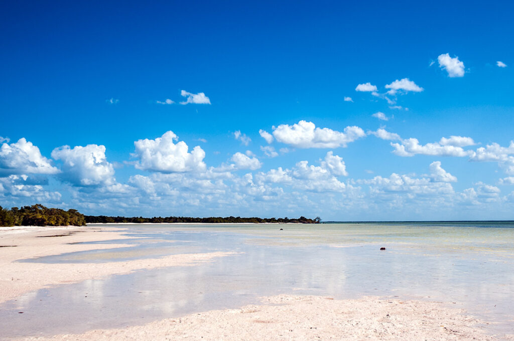 Wide sandy beach in Puerto Morelos with calm Caribbean water and blue sky.