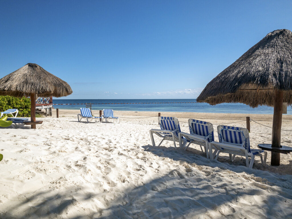 White-sand beach with lounge chairs and palapa umbrellas beside the Caribbean Sea in Puerto Morelos.