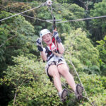 A person ziplining through lush jungle, wearing a helmet and harness, with an excited expression.