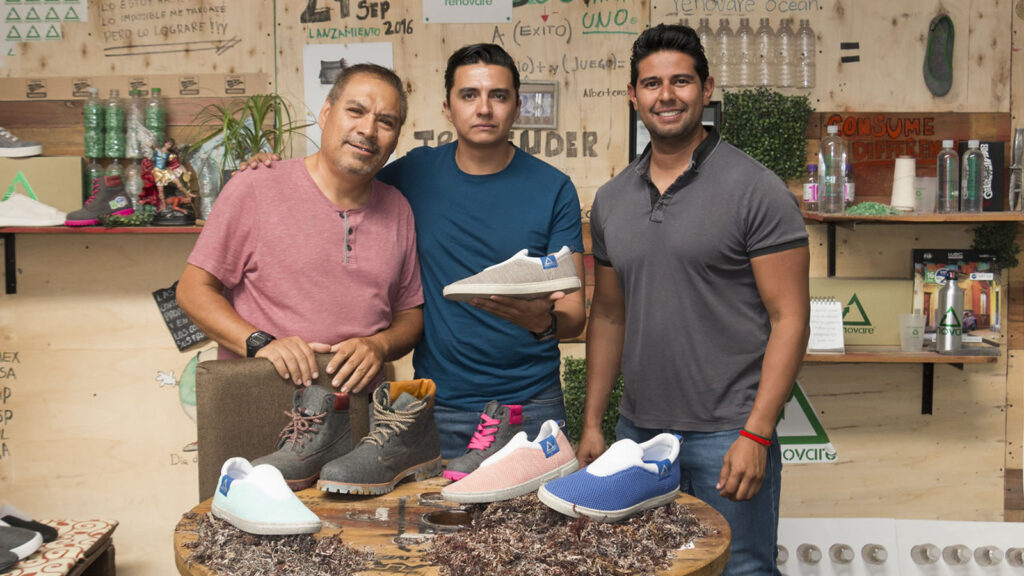 Three inventors standing in front of a collection of shoes made out of sargassum.