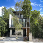 A modern, multi-story house surrounded by lush greenery with a sleek architectural design and large windows.