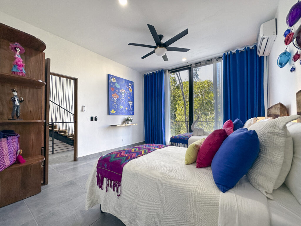 A colorful bedroom with bright decor, traditional Mexican art, and a large window.