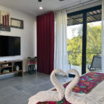 A bedroom with heart-shaped towel swans on the bed, a large TV, and sliding doors leading to a balcony.