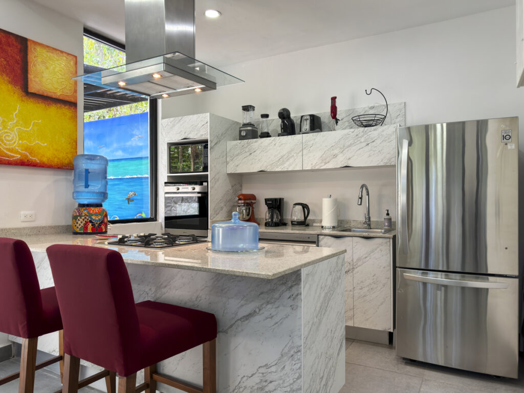 A bright, modern kitchen with marble countertops, a stainless steel refrigerator, and colorful decor.