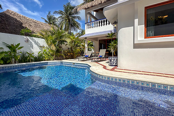 A bright pool with blue mosaic tiles beside a tropical vacation home