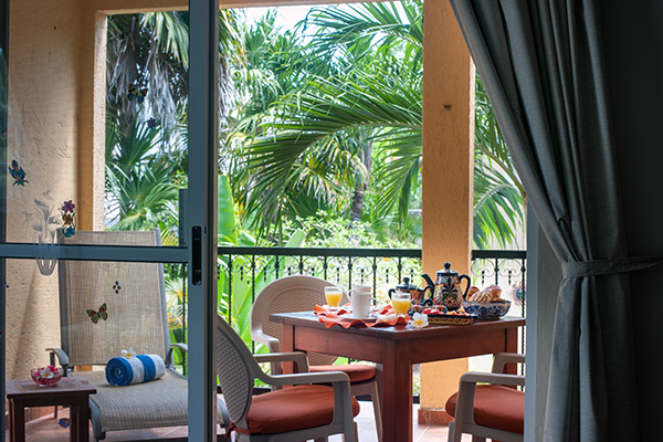 A cozy balcony with a breakfast table set for two, surrounded by tropical palm trees.