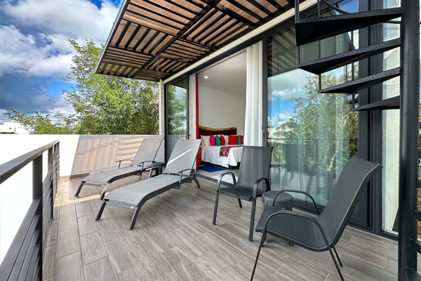 A spacious balcony with lounge chairs and a shaded roof, connected to a bedroom with sliding glass doors.