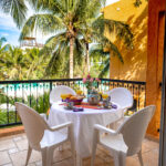 Table set on a balcony with views of palm trees and a garden.