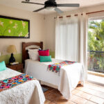 Bedroom with two twin beds, colorful pillows, and balcony access.