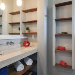 A modern bathroom with a double sink vanity, open wood shelving, and rolled towels, accented by soft lighting and elegant design.