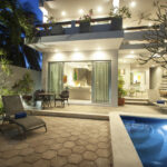 The exterior of Casa Agua Azul at night, showcasing a well-lit patio, pool area, and large sliding doors leading into the living room.