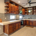 A modern kitchen with dark wood cabinetry, mosaic backsplash, stainless steel appliances, and open shelving.