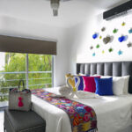 bright bedroom featuring a plush bed with colorful throw pillows, a decorative embroidered blanket, and a wall adorned with vibrant glass heart ornaments.