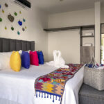 A bedroom with a king-size bed adorned with colorful throw pillows, a vibrant embroidered blanket, and swan-shaped towels, with decorative glass hearts on the wall.