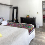 A bright bedroom featuring a king-size bed with colorful pillows, an embroidered blanket, and sliding glass doors leading to the rooftop terrace.