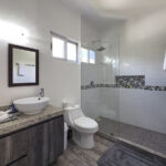 A modern bathroom with a granite countertop, double vessel sinks, a walk-in glass shower, and decorative black and white tile accents.