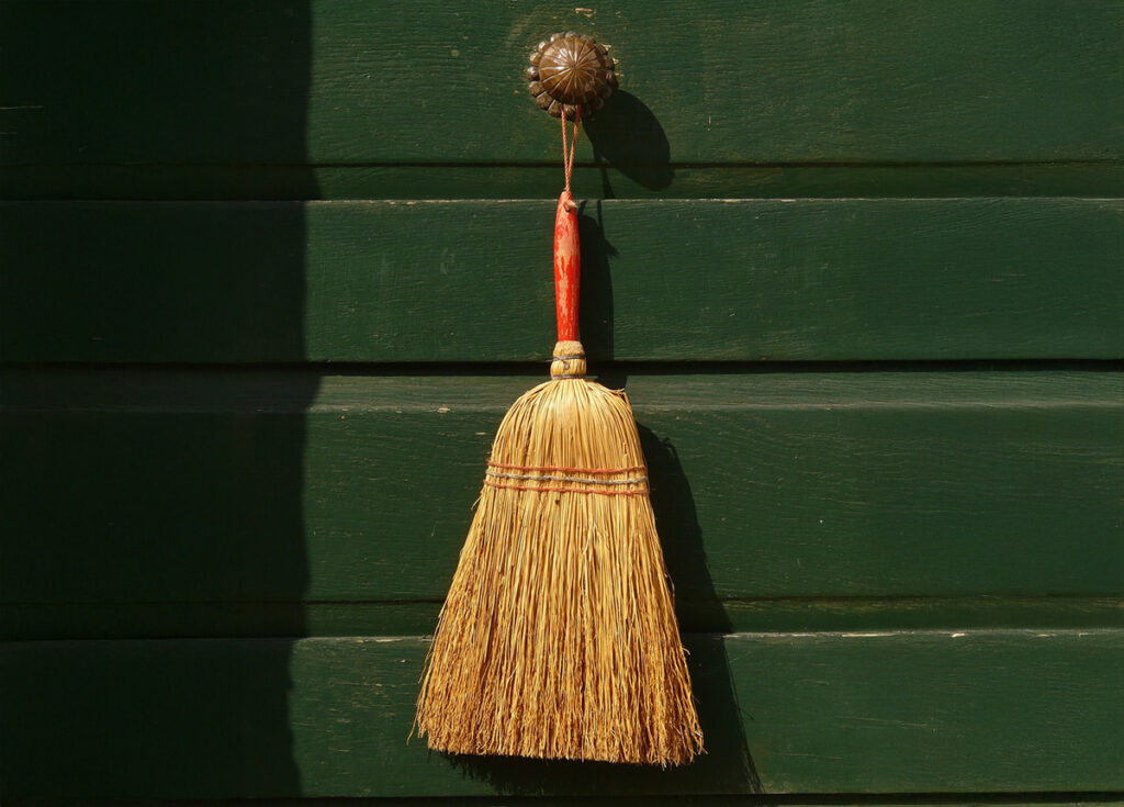 A minimalist and rustic depiction of a straw broom hanging on a green wooden door. This image highlights the cultural practice of using a broom as a tool for symbolic renewal during New Year’s celebrations in Mexico. It emphasizes the theme of cleansing and letting go of the past.