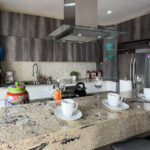 A close-up view of a modern kitchen with sleek dark cabinetry, a polished stone countertop, and colorful Mexican accents, including a vibrant ceramic jar.