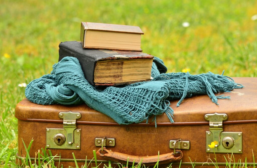 A whimsical composition featuring a vintage suitcase, scarf, and books, set against a natural backdrop. This image highlights the Mexican New Year’s tradition of walking with a suitcase at midnight to invite travel and exploration in the coming year. It captures the spirit of wanderlust and fresh opportunities.