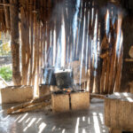 Traditional Maya outdoor kitchen with a wood-burning fire, smoke rising through wooden slats, and rustic stone seating.