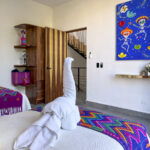 Bright and colorful bedroom featuring traditional Mexican decor, a towel swan on the bed, a vibrant Day of the Dead painting, and handcrafted wooden furnishings.