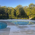 Serene outdoor swimming pool surrounded by lush jungle greenery, featuring lounge chairs and a stone pathway.