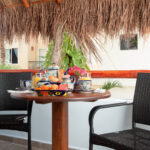 A cozy outdoor breakfast setup on a private balcony under a palapa roof, with tropical greenery in the background.A cozy outdoor breakfast setup on a private balcony under a palapa roof, with tropical greenery in the background.