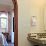 A beautifully tiled bathroom vanity with a decorative sink, leading into a cozy bedroom with soft lighting and a serene ocean-inspired decor.