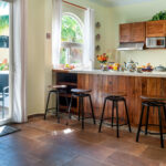 A bright and spacious kitchen with a wooden breakfast bar, barstools, and a sliding door leading to an outdoor dining area.