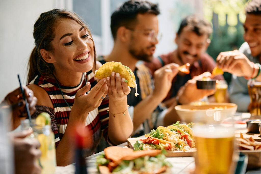 A group of friends enjoying a meal together, with a woman smiling as she holds a taco.