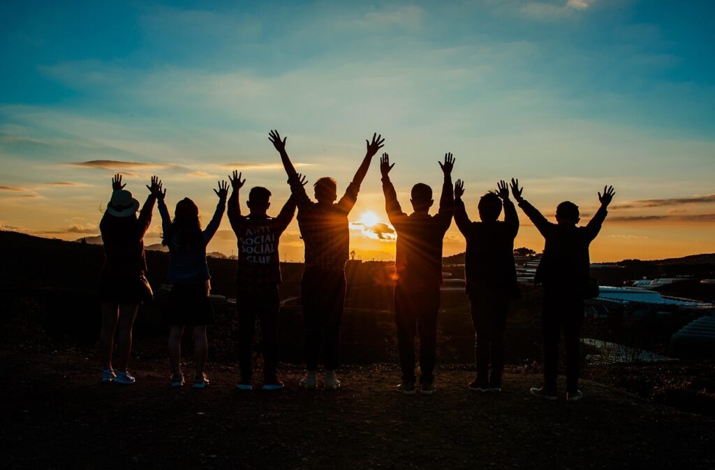 A group of friends raising their hands in celebration, silhouetted against a beautiful sunrise.