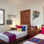 Casa Zarah twin bedroom with colorful bedding, wooden shutters, and hand-carved nightstand.