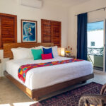Casa Zarah bedroom with king bed, colorful pillows, wood shutters, and balcony access.