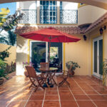 Casa Zarah courtyard with terracotta tile, red umbrella, and tropical plants.