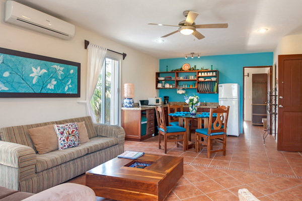 Bright living and dining area with striped sofa, wooden table and chairs, and turquoise accent wall.