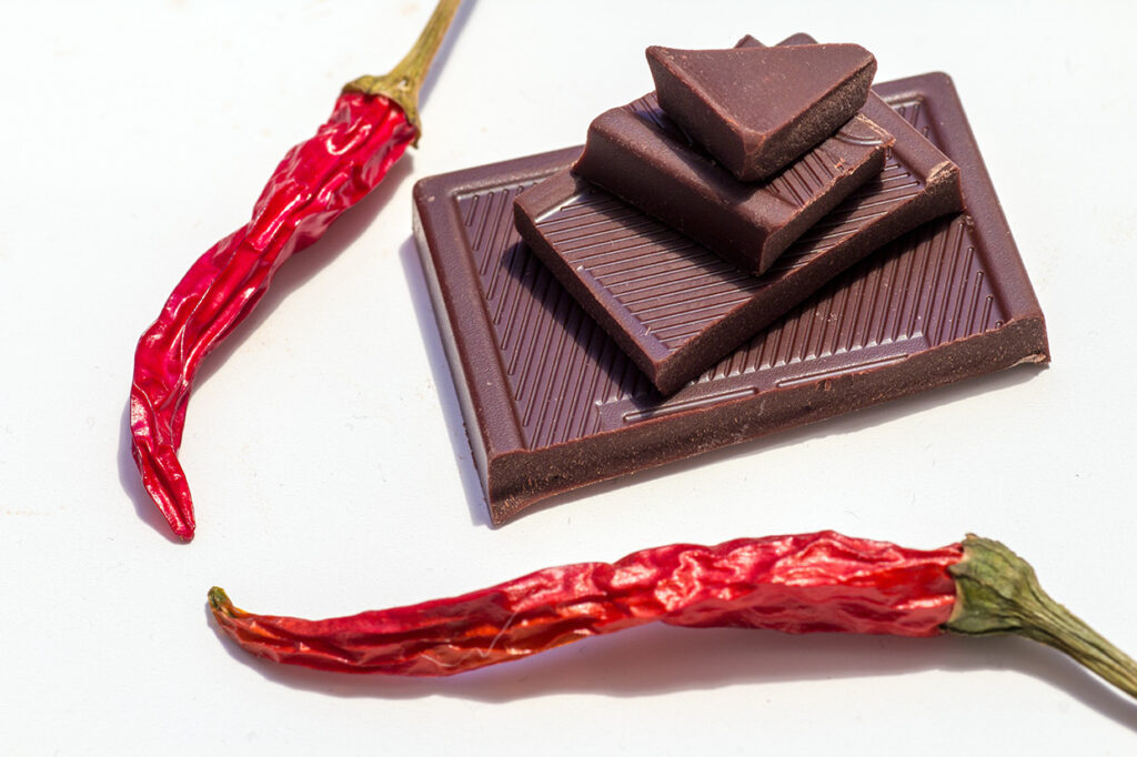 Dark chocolate pieces with dried chili peppers on a white background
• Title: Chocolate with a Kick: Tradition Meets Heat