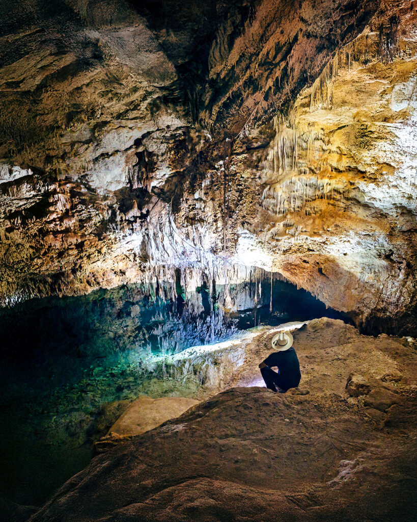 Person sitting beside a crystal-clear cenote inside a cave