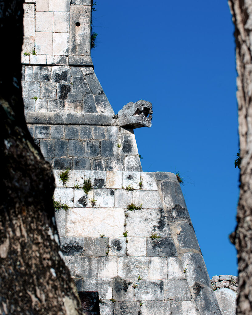 Side view of El Castillo pyramid with serpent head and trees in foreground