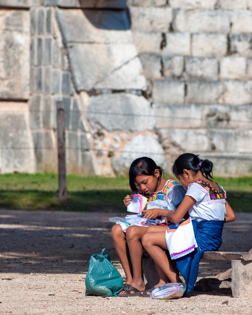 Two Maya girls in traditional clothing sitting at Chichén Itzá