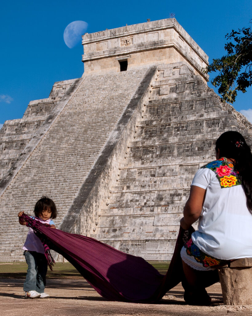 Woman and child in front of El Castillo pyramid at Chichén Itzá with moon above