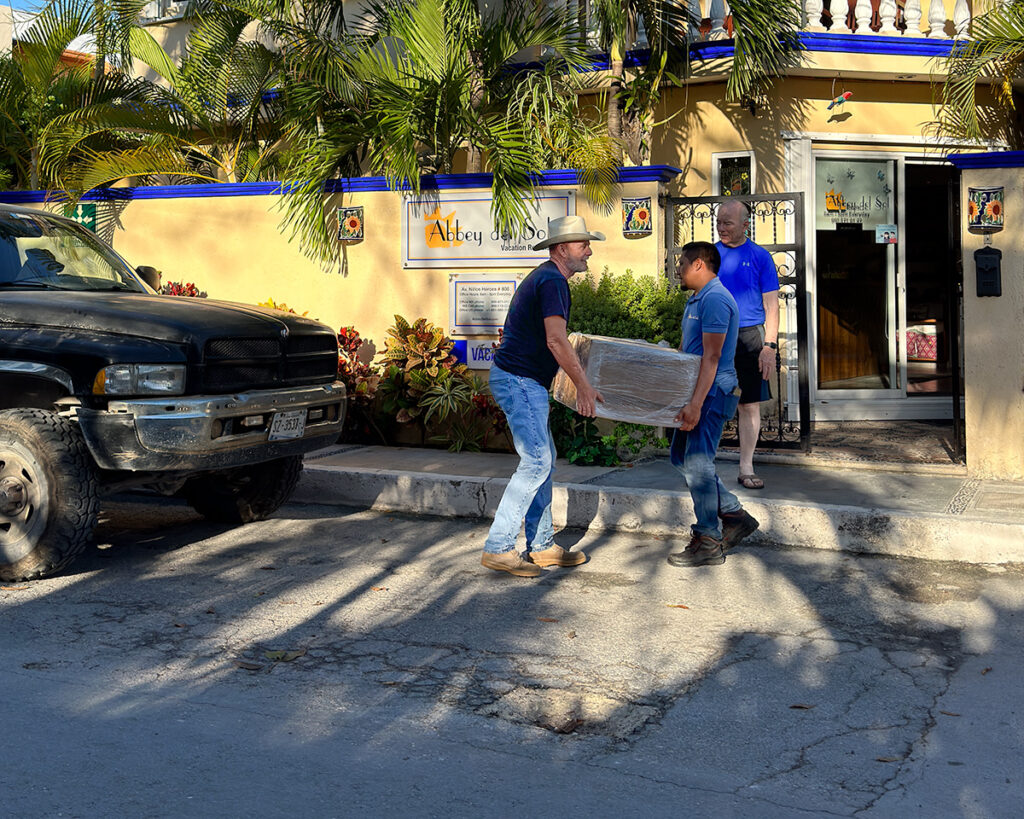 Two men carrying a box outside Abbey del Sol
