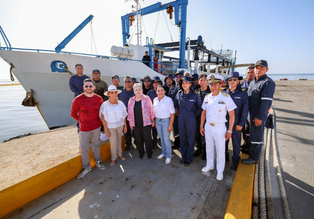 Officials and naval crew stand together in front of a sargassum-collecting vessel in Puerto Morelos, Mexico.