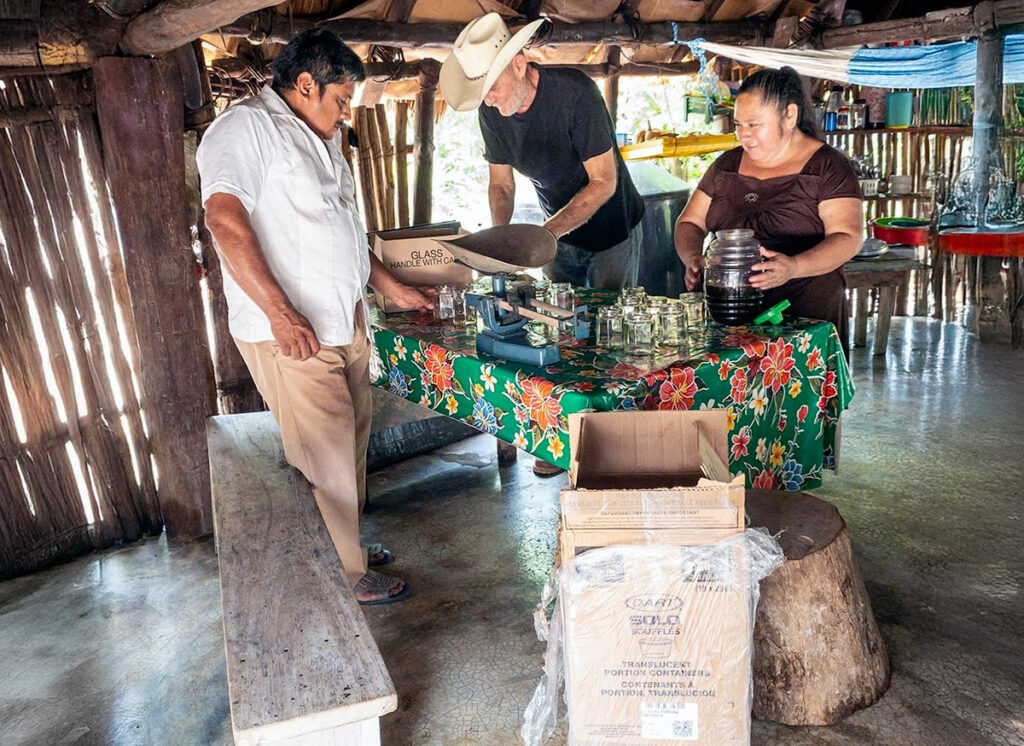 Three people prepare honey jars inside a traditional Maya home