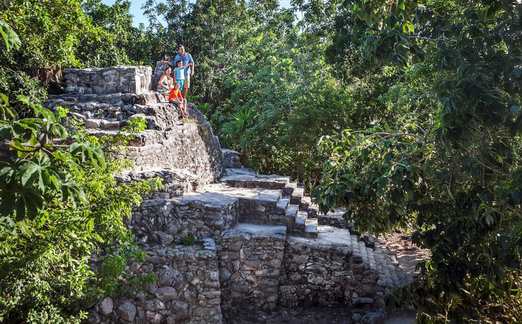 Visitors stand atop a restored stone structure surrounded by dense jungle at Xcaret.