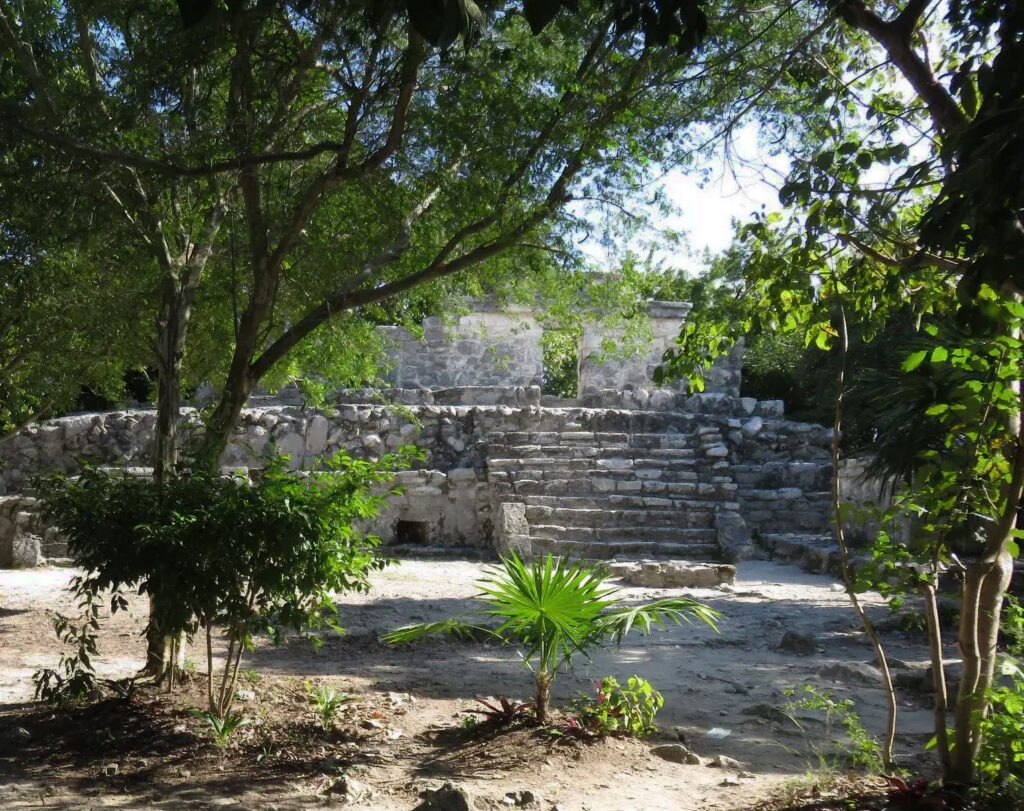 Restored Maya stone structure partially shaded by trees at Xcaret.

