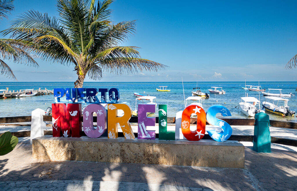 Colorful Puerto Morelos sign with fishing boats and turquoise Caribbean Sea in the background.