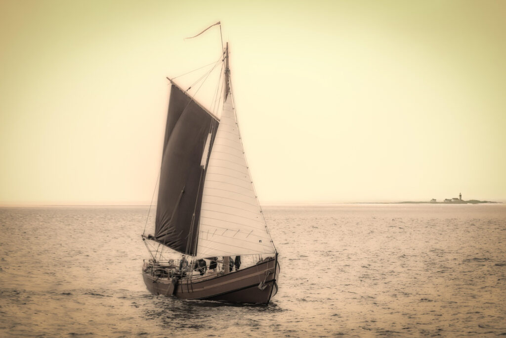 Sepia-toned image of a traditional sailboat at sea, carrying goods across calm waters.