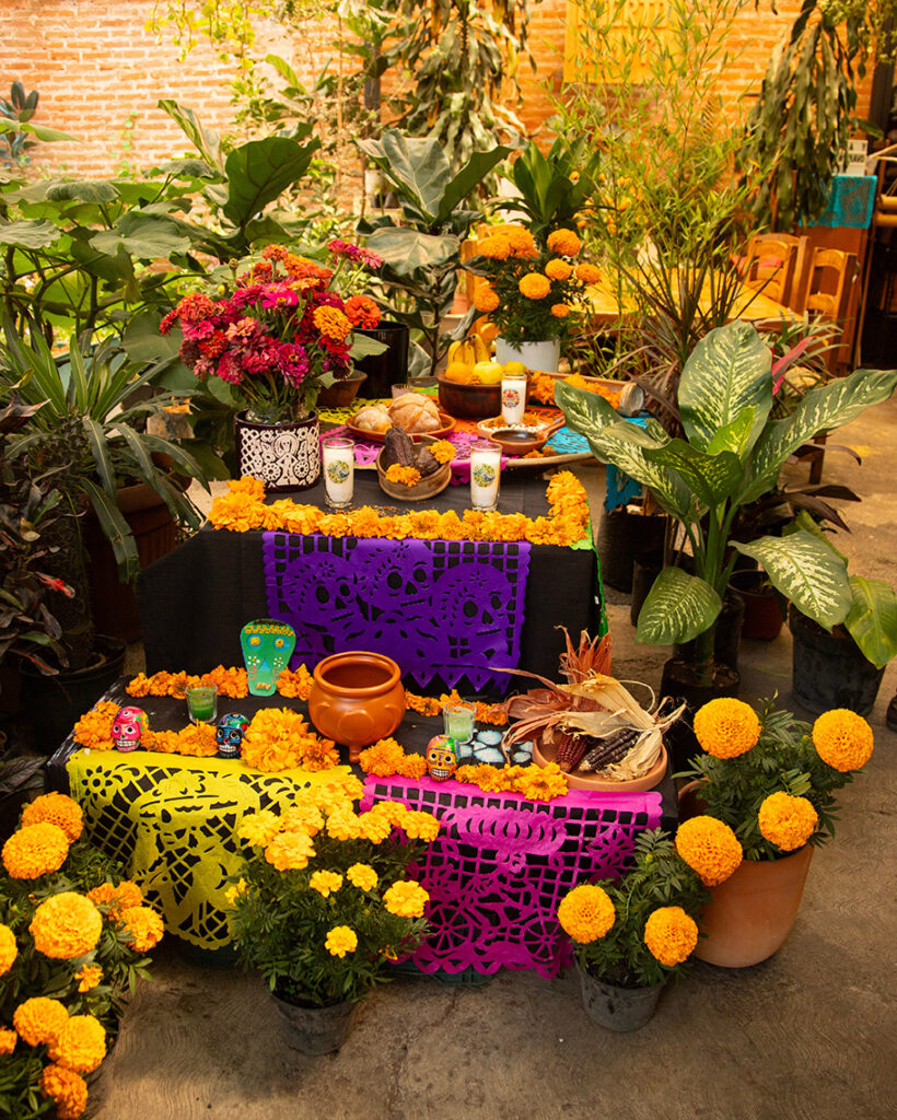 Colorful Día de Muertos altar decorated with marigolds, papel picado, candles, and offerings.