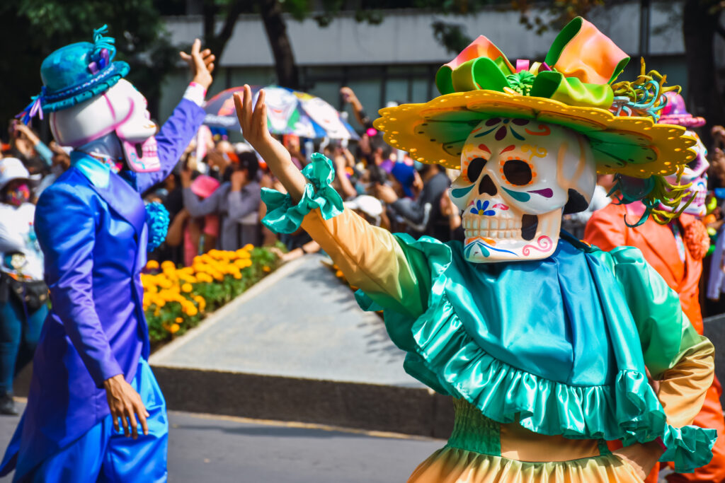 Parade performers dressed as colorful Catrinas waving to the crowd in Puerto Morelos, Mexico.